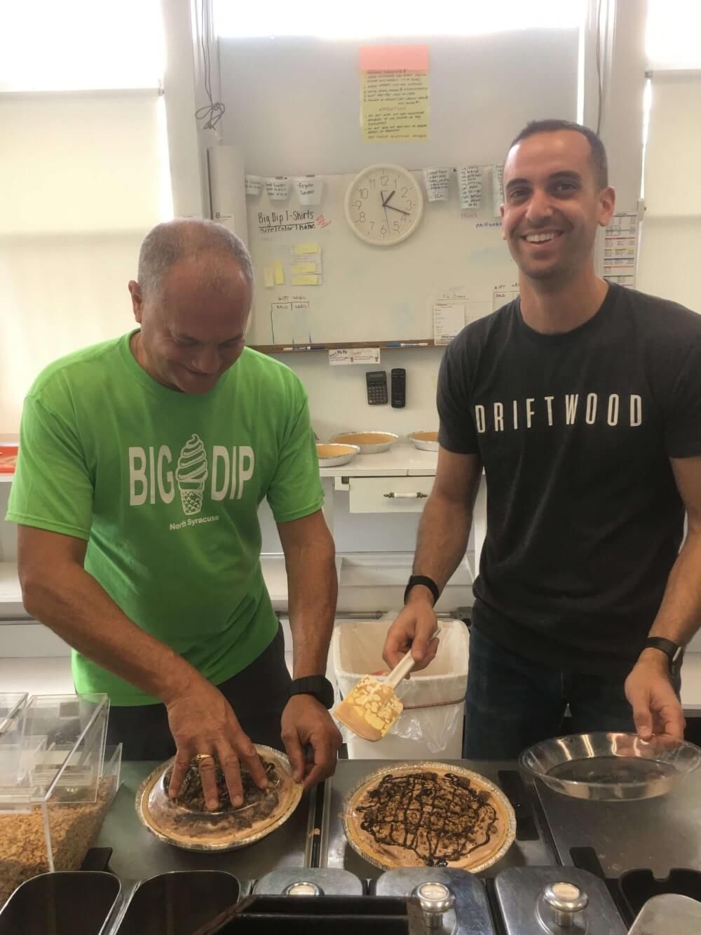 A man wearing a green shirt that says big dip is standing next to another man wearing a black shirt that says driftwood