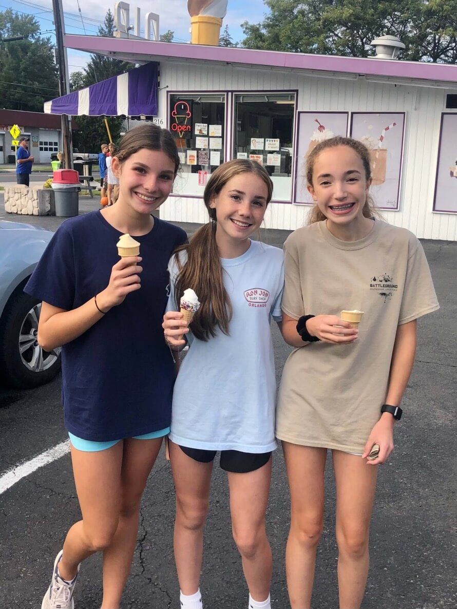 Three young girls are standing in front of an ice cream shop holding ice cream cones.