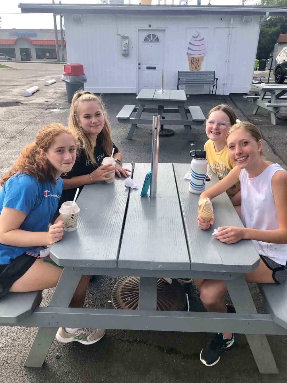 A group of young girls are sitting at a picnic table eating ice cream.