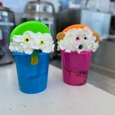Two cups of ice cream with whipped cream on top are sitting on a table.