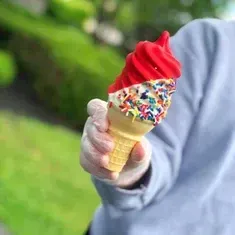 A person is holding a red ice cream cone with sprinkles.