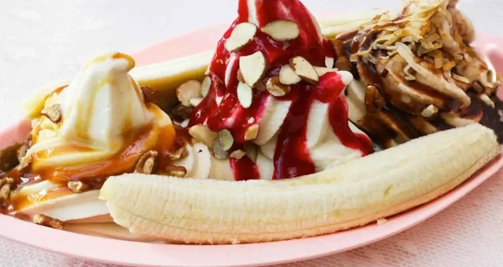 A banana split with ice cream and sauce on a pink plate.