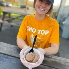 A woman in a yellow shirt is holding a bowl of ice cream.