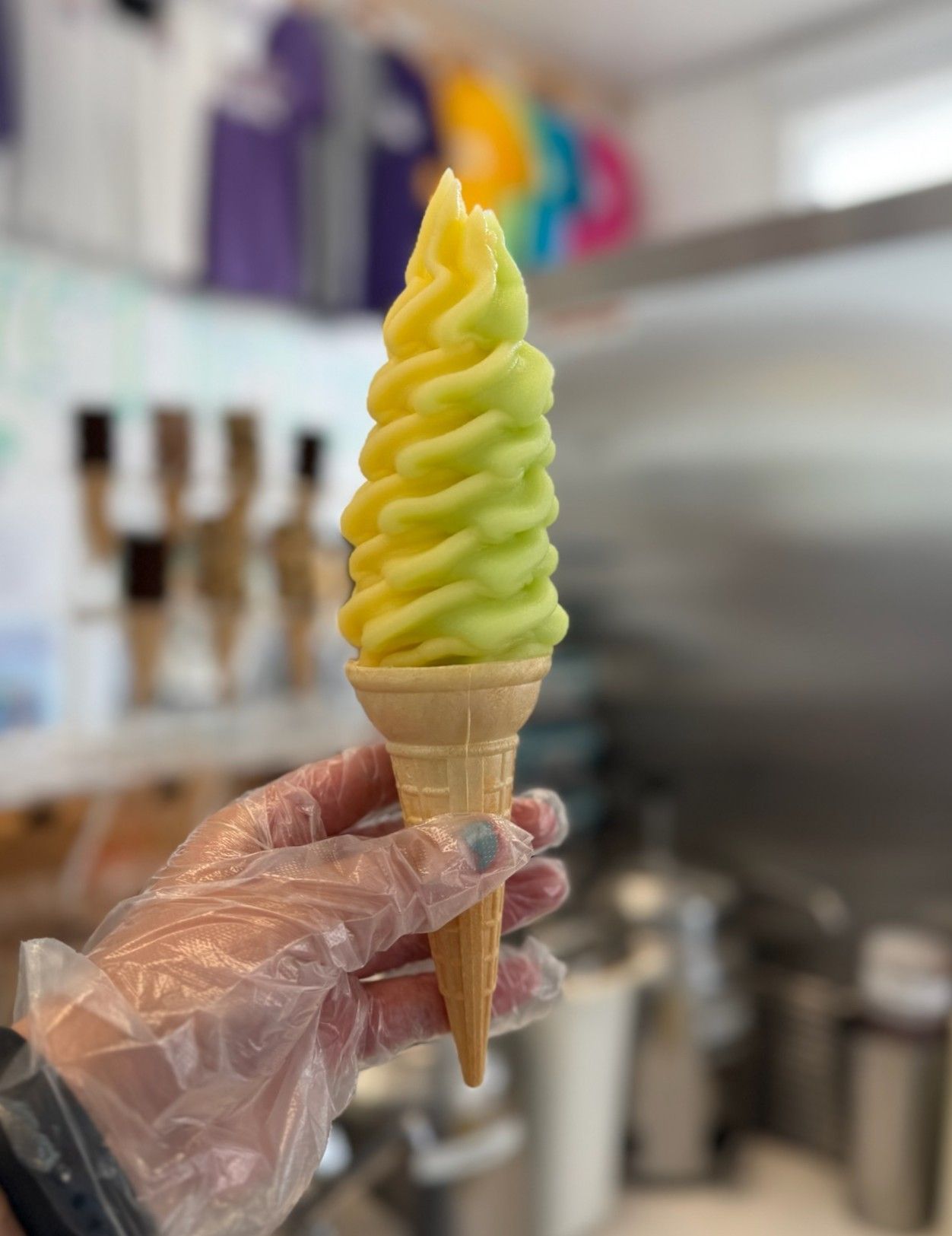 A person wearing plastic gloves is holding a soft serve ice cream cone.