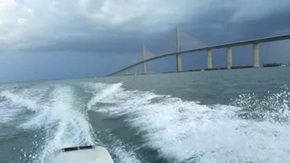 A boat is going under a bridge in the ocean.