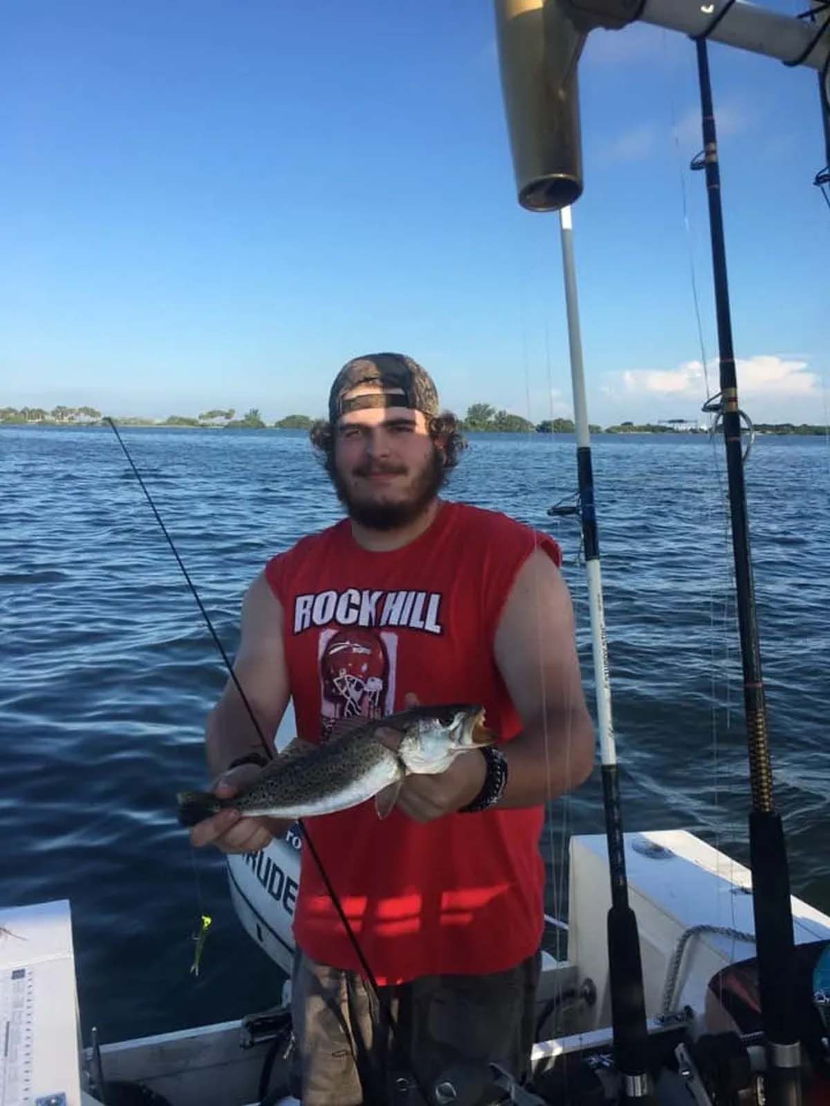 A man in a rock hill shirt is holding a fish on a boat.