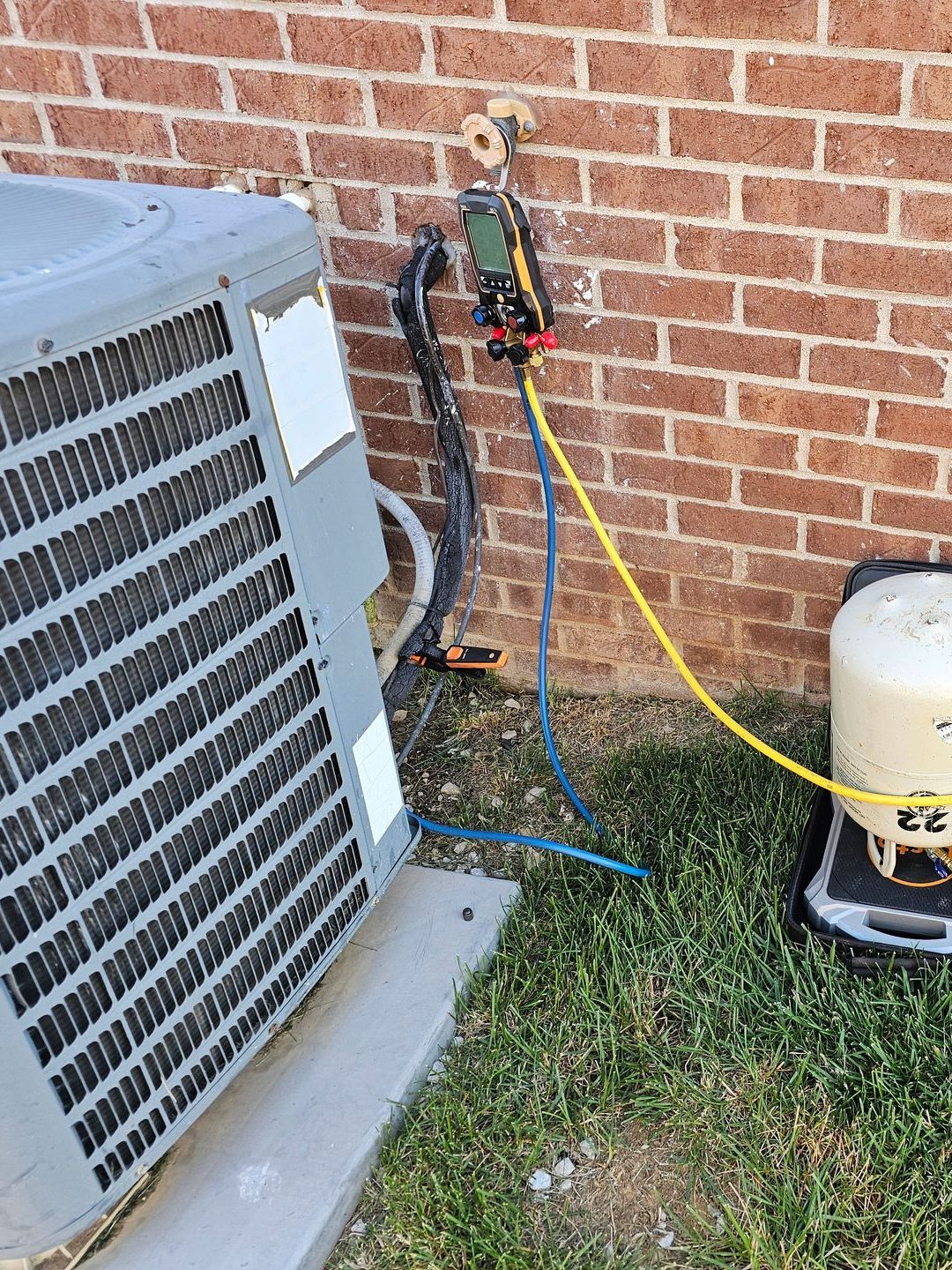 An air conditioner is being serviced outside of a brick building.