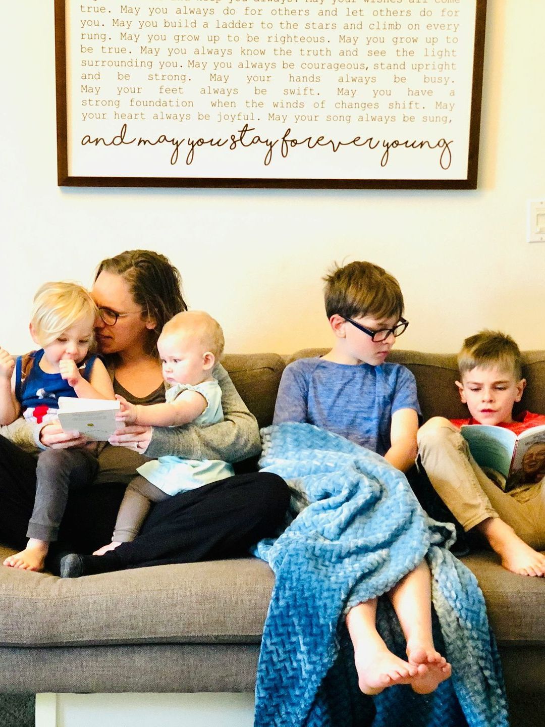 A woman and three children are sitting on a couch reading books.