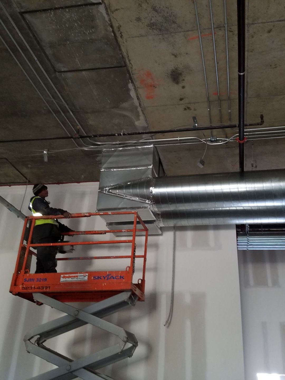 A man is standing on a scissor lift working on a ceiling.