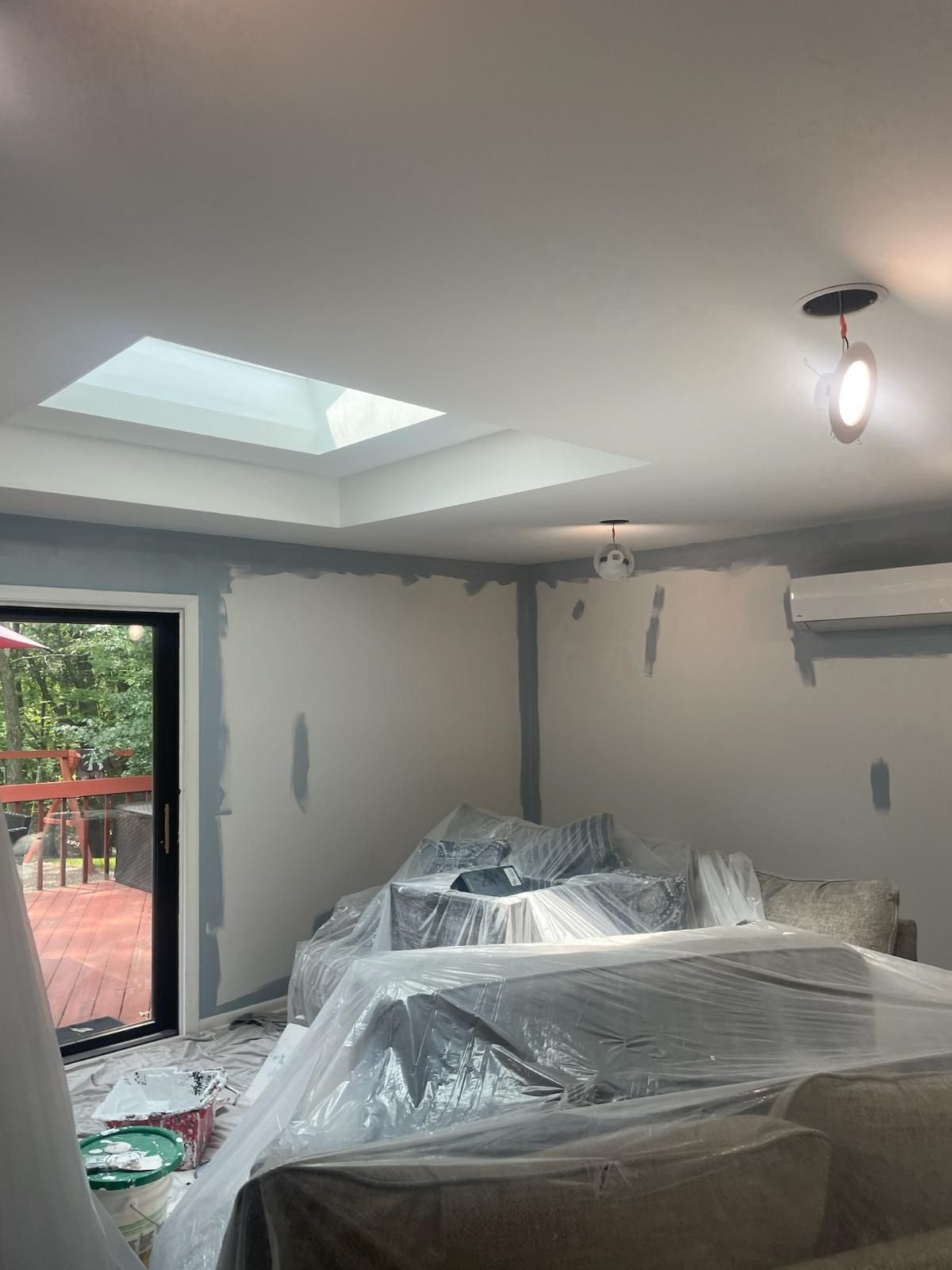 A living room with a couch covered in plastic and a skylight.