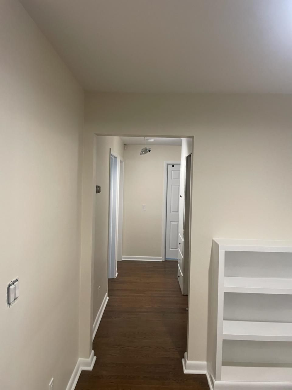 A hallway with a bookshelf in the middle of it leading to a bedroom.