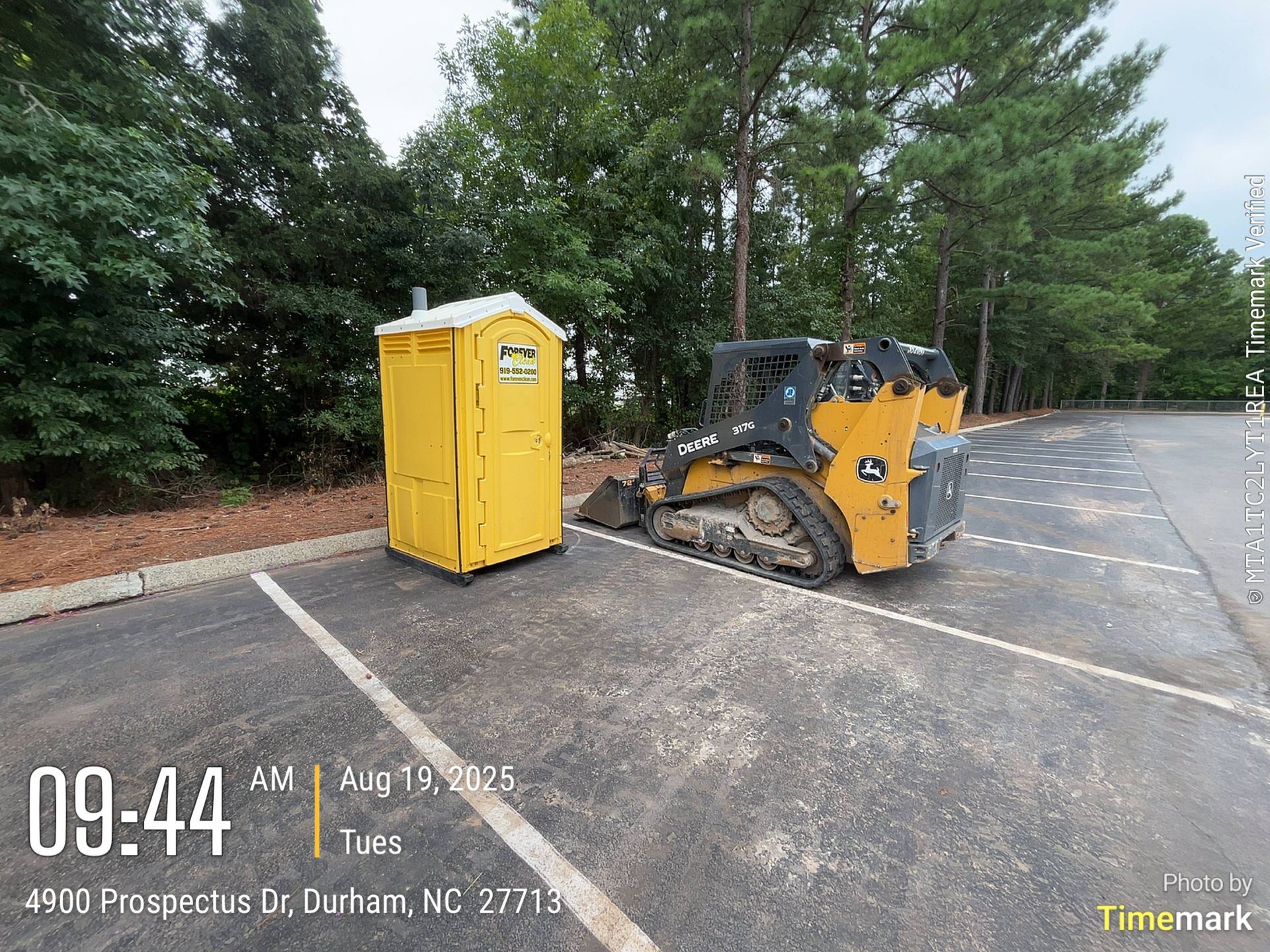 Yellow portable toilet and yellow skid steer loader parked in a parking lot in Durham, NC.