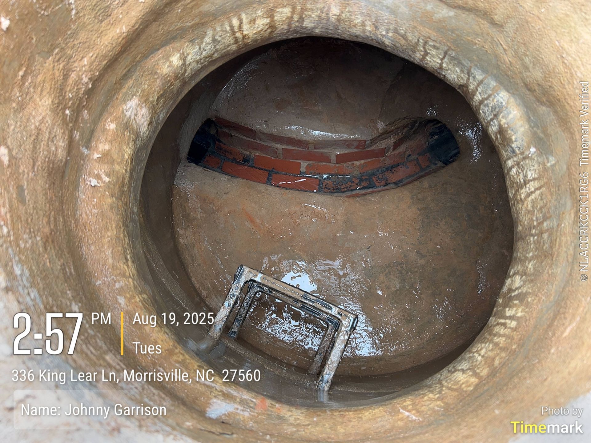 Interior view of a well. Shows a brick arch at the top, a ladder, and a partially filled basin.