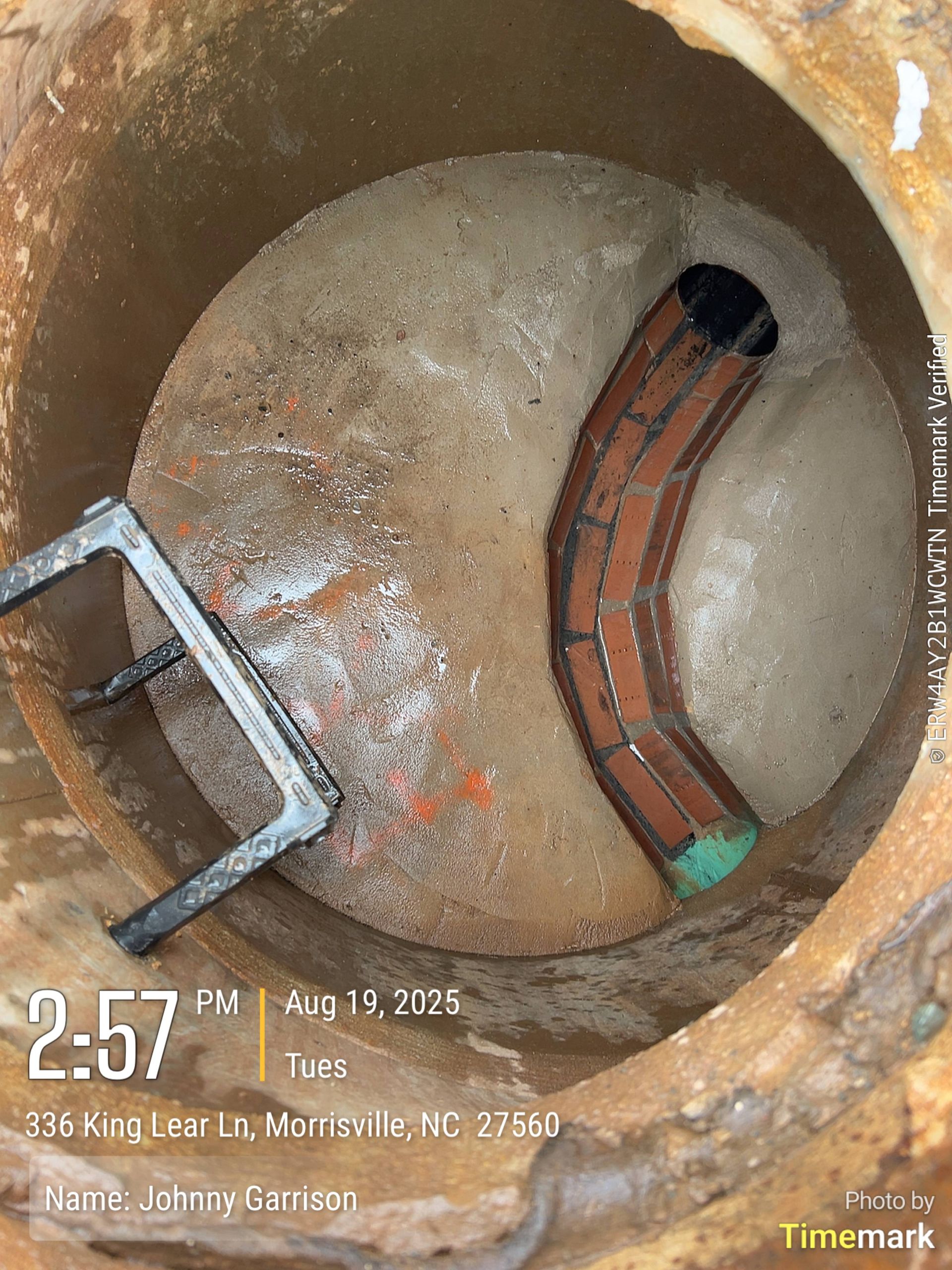 Inside a manhole: bent brown pipe, metal frame, debris, with timestamp.