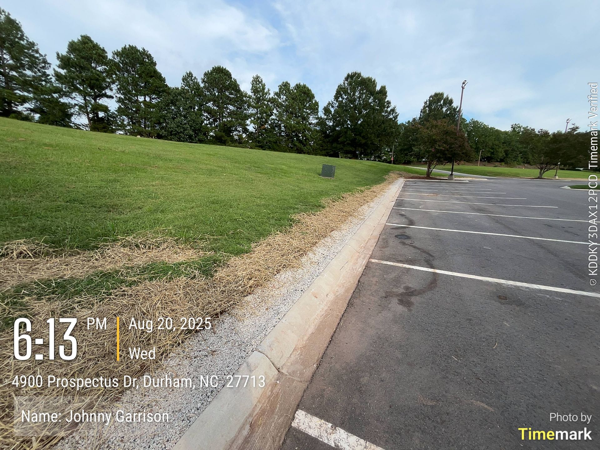 Grassy hill beside a parking lot with trees in the background under a cloudy sky.
