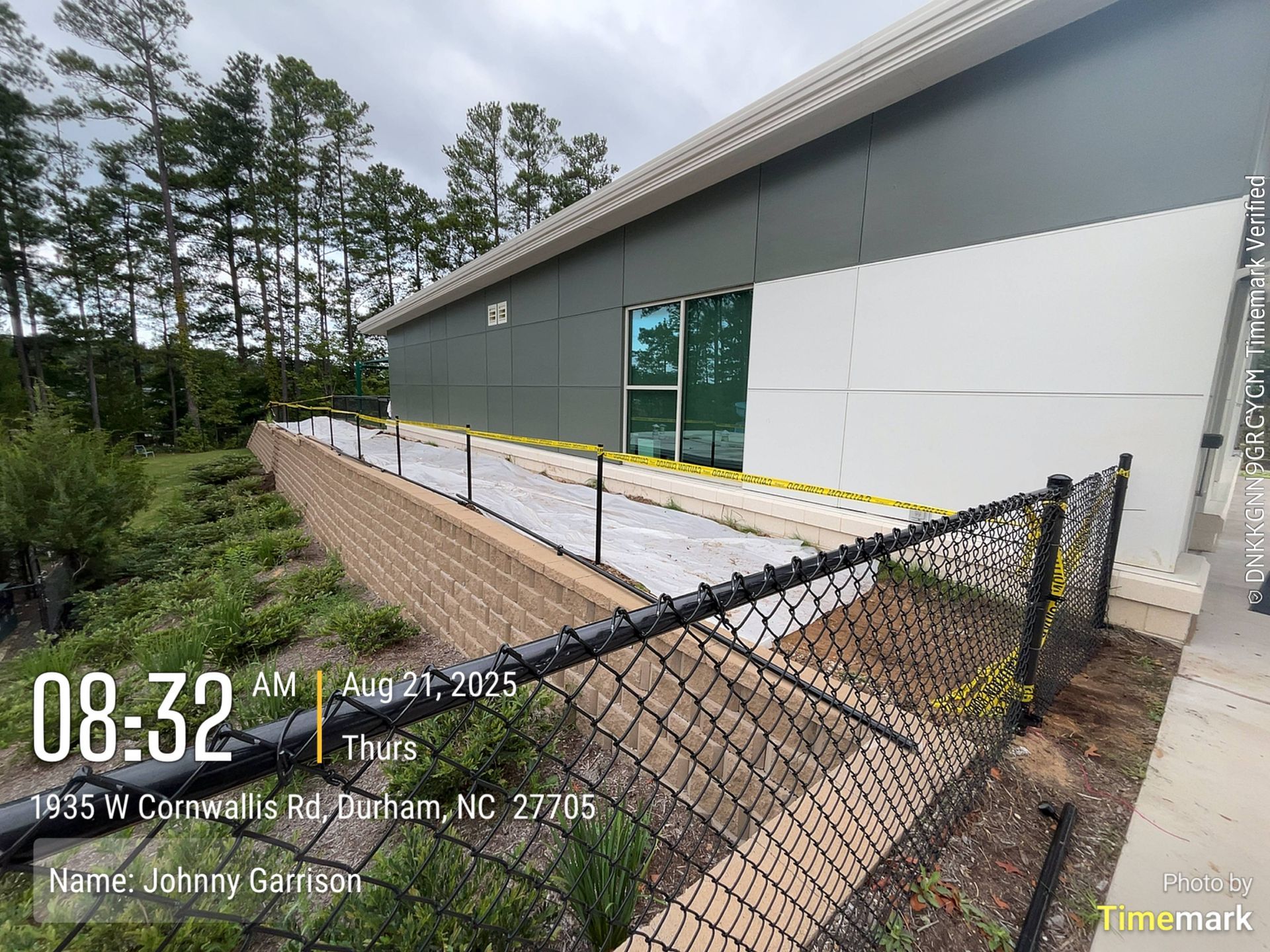 A building with a ramp, black fence, and retaining wall. Trees and foliage in the background.