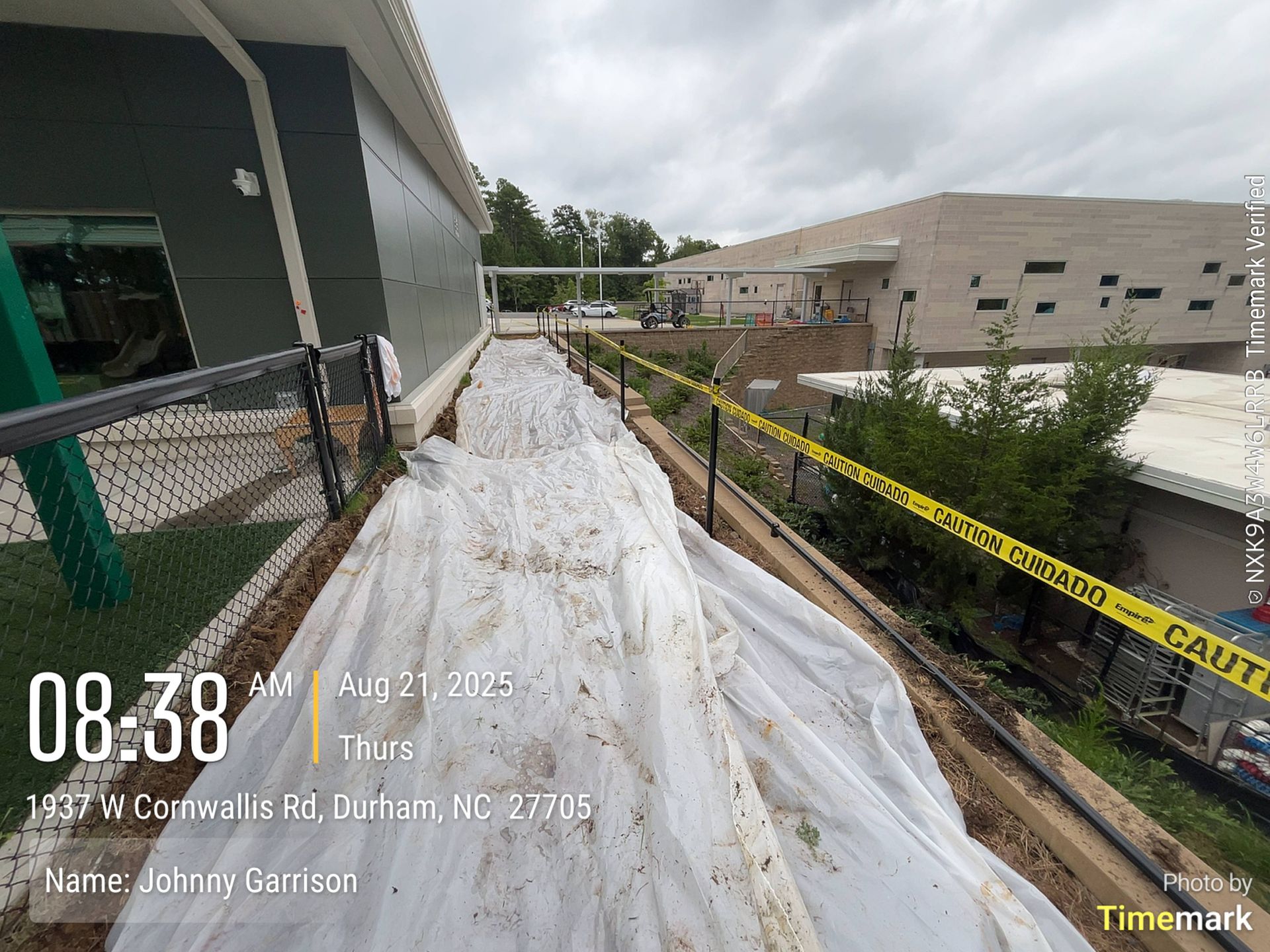 Construction site, white tarp covering ground along building. Yellow caution tape, time/date stamp visible.