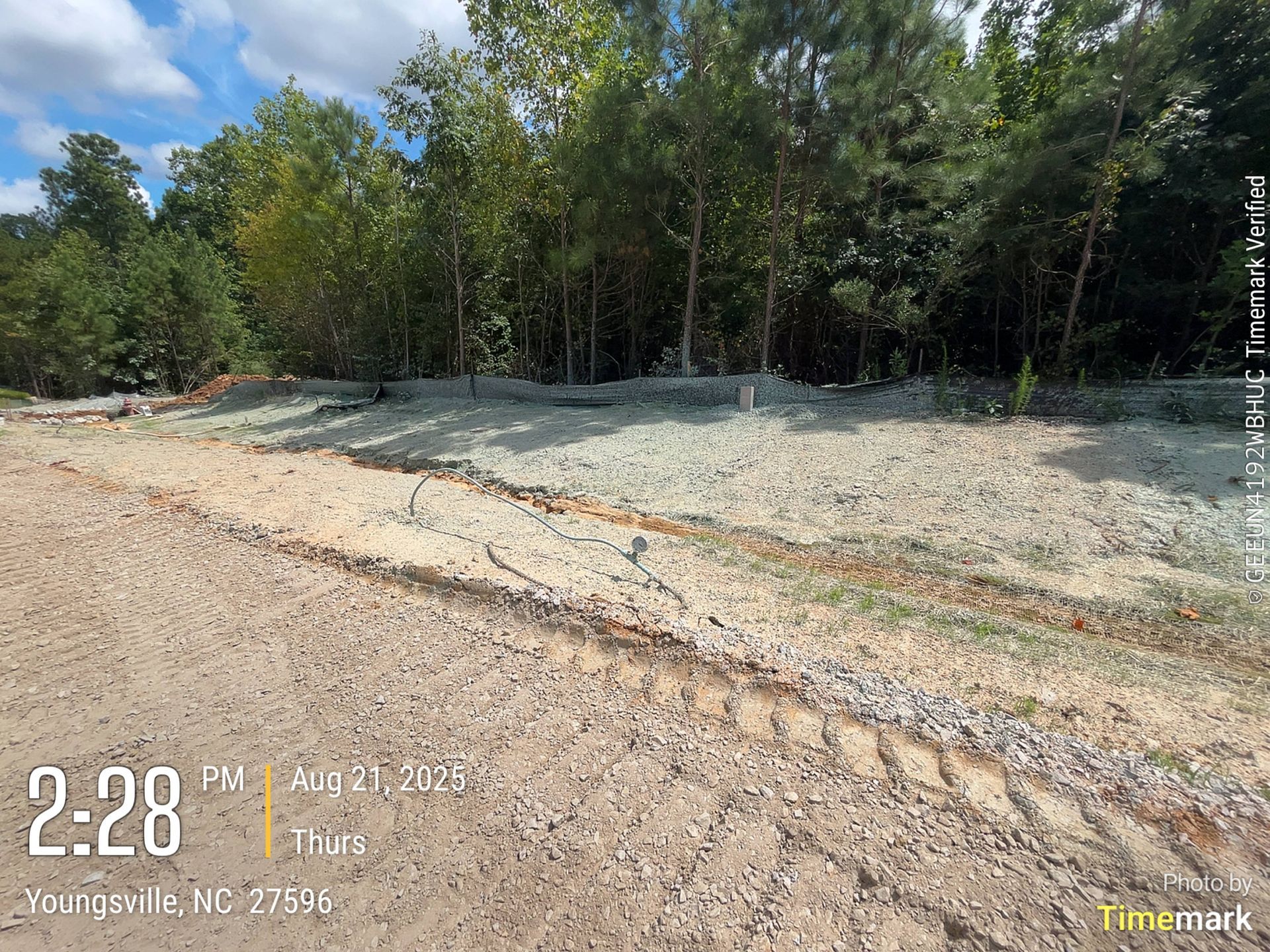 A dirt road leads to a cleared area with gravel and trees under a cloudy sky in Youngsville, NC.