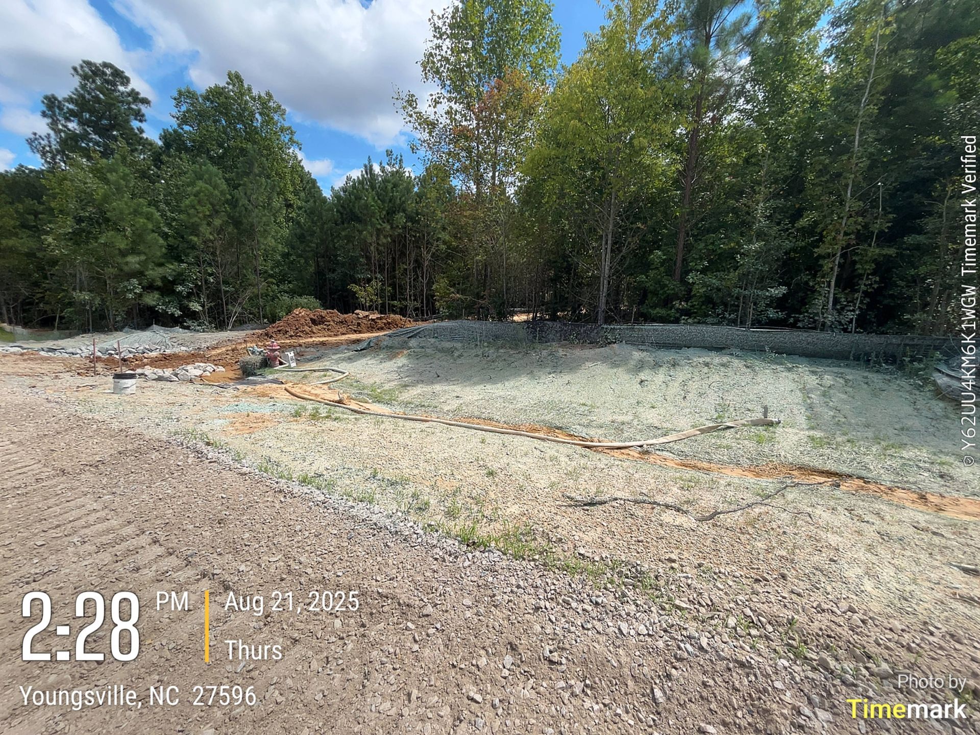 Dirt lot with a pile of dirt in the center, trees in the background, blue sky, 2:28 PM.