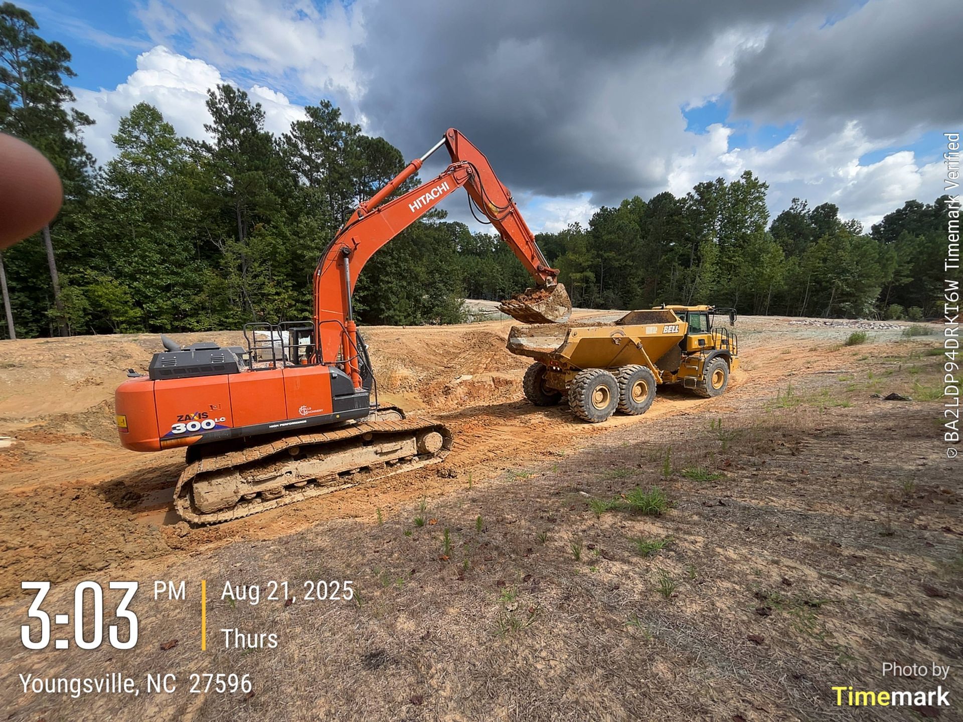 An orange excavator loading dirt into a yellow dump truck at a construction site.