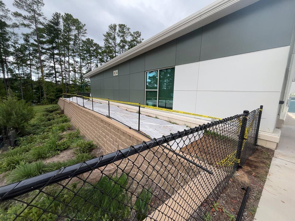 Exterior of a building with a ramp, fence, and retaining wall. Trees in the background under a cloudy sky.