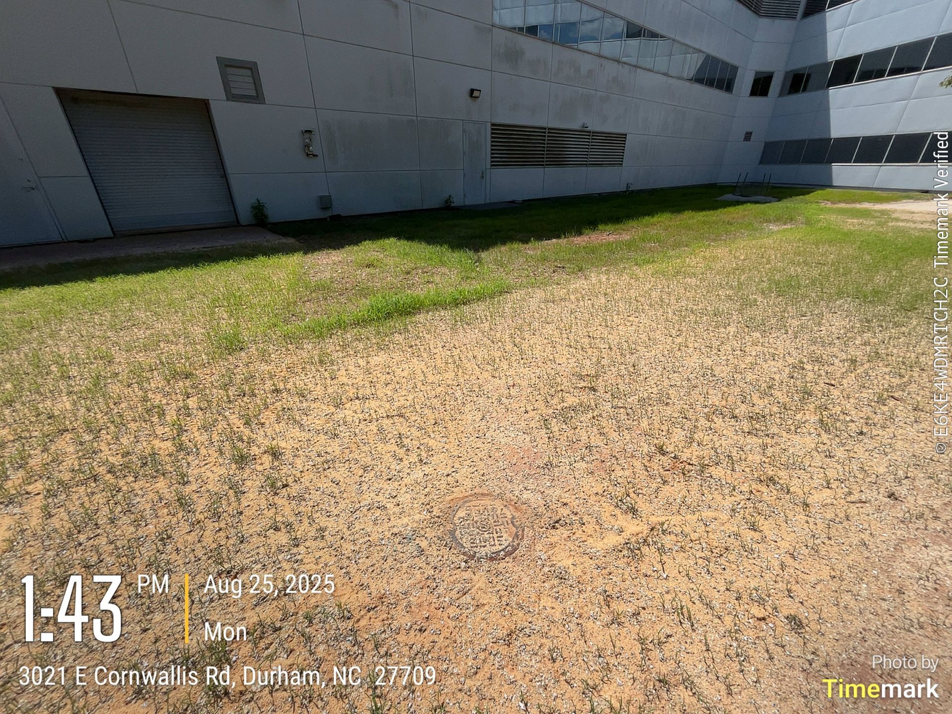 A building exterior with a partially grassy, brown yard. Time and location stamp in the corner.
