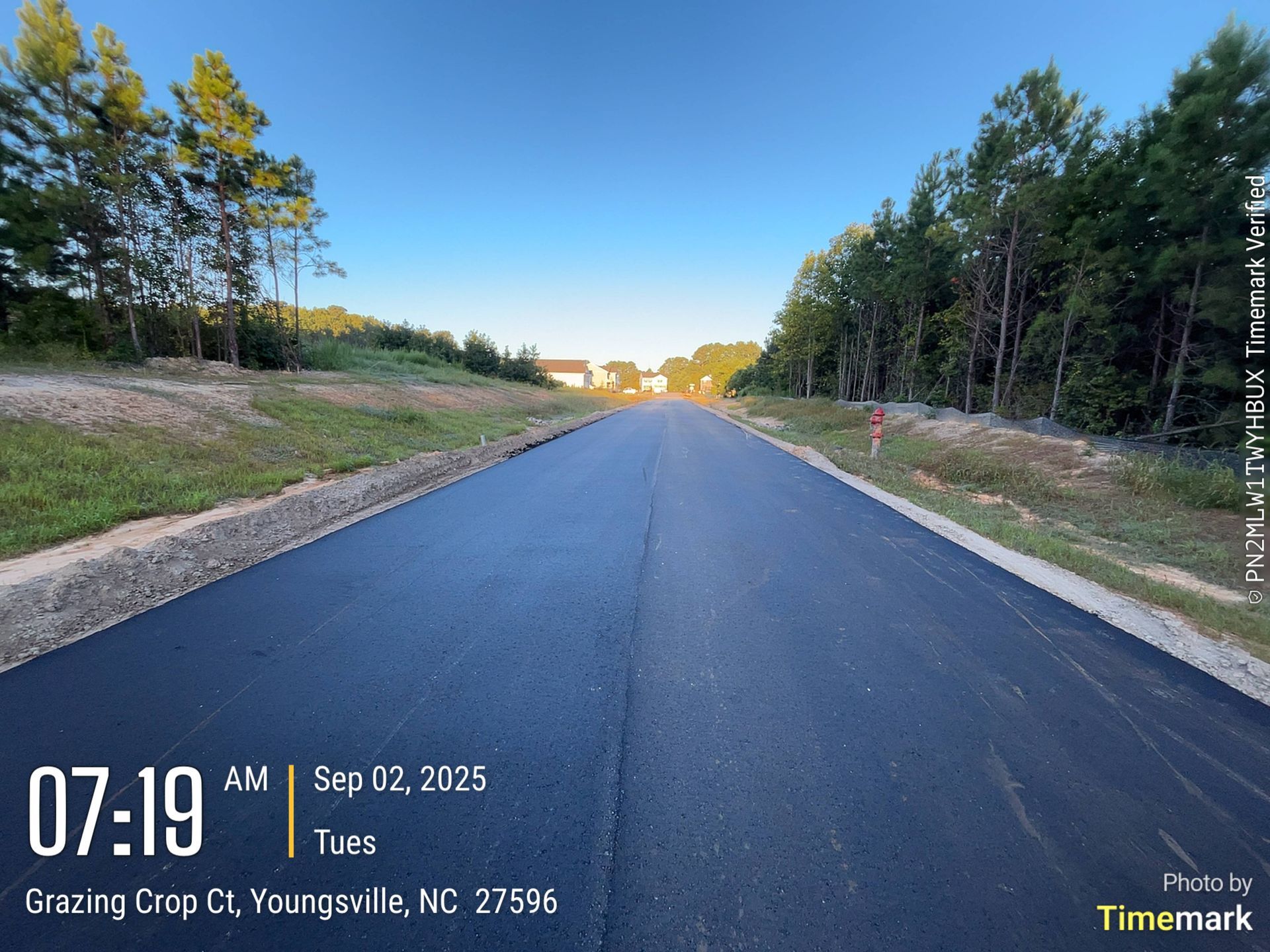 Newly paved road, Grazing Crop Ct, Youngsville, NC, under blue sky at 7:19 AM, Sep 02, 2025. Trees line the sides.
