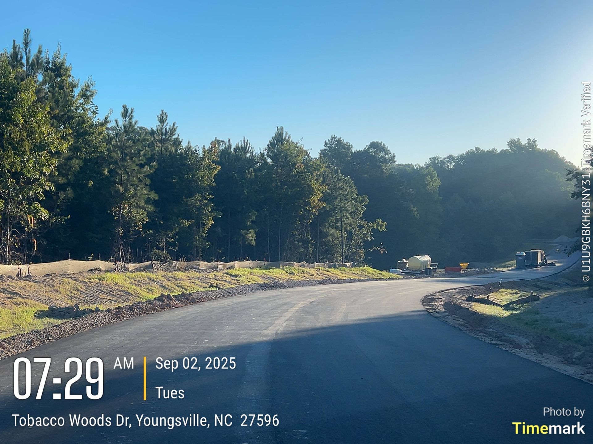 Newly paved road in Youngsville, NC, with construction equipment and trees under a clear sky.