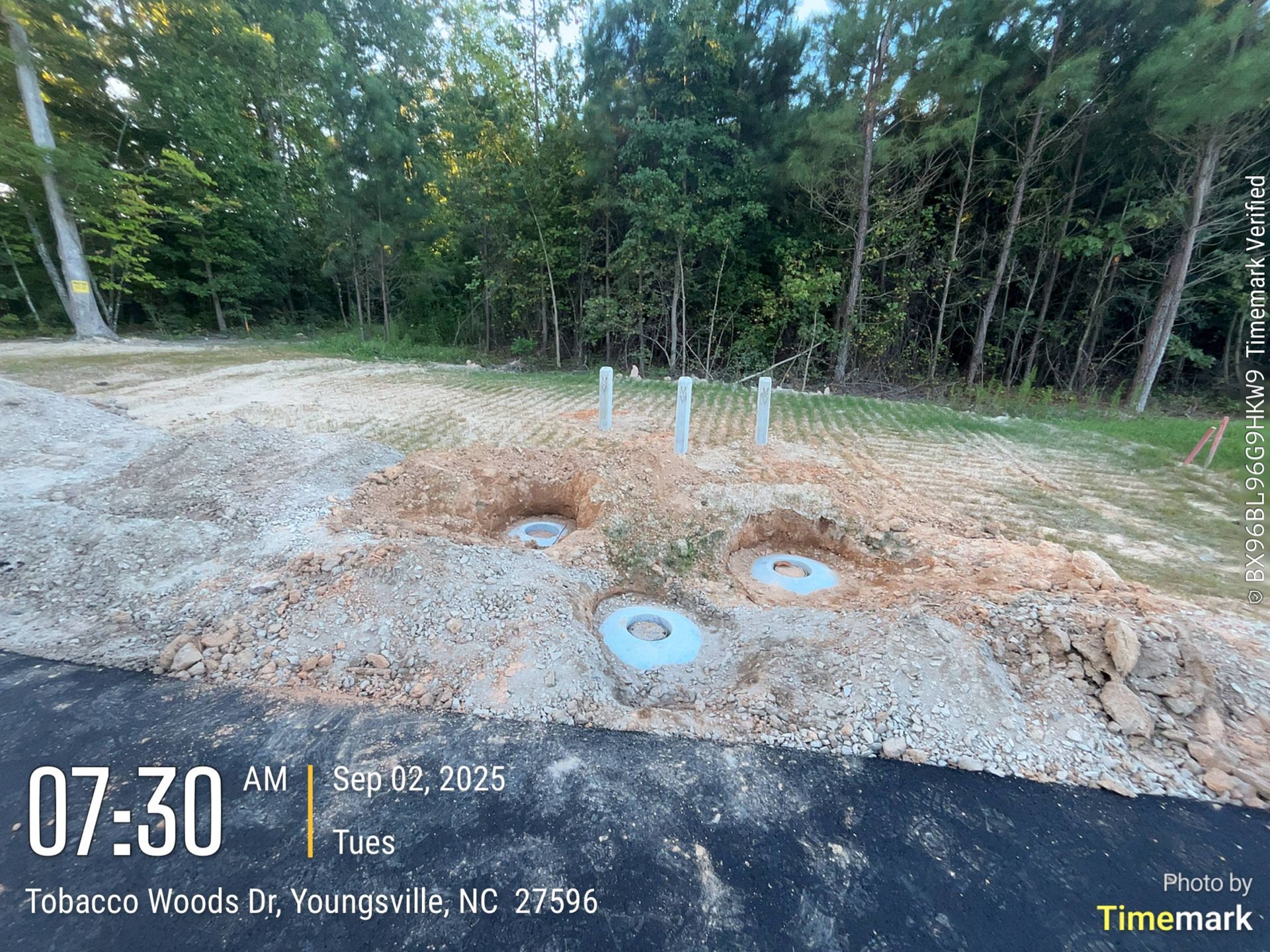 Construction site: dirt, pipes, and concrete rings with trees in the background, in Youngsville, NC.