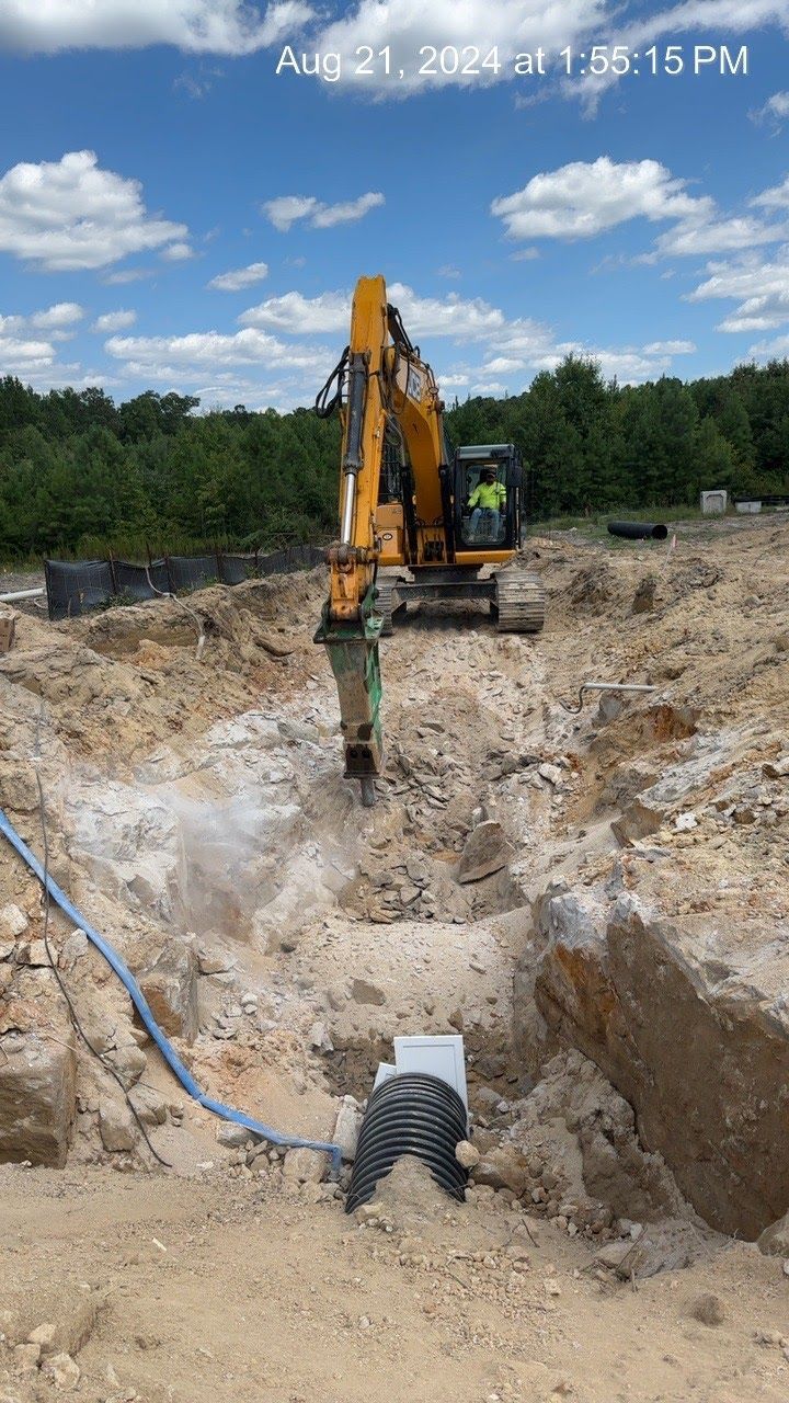 Excavator breaking ground on construction site. Blue sky, yellow machine, dirt, and a pipe visible.