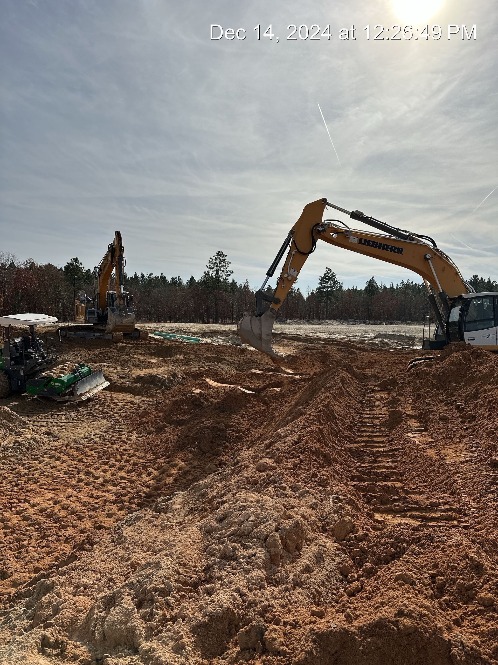 Construction site with two excavators digging in dirt under a sunny sky.