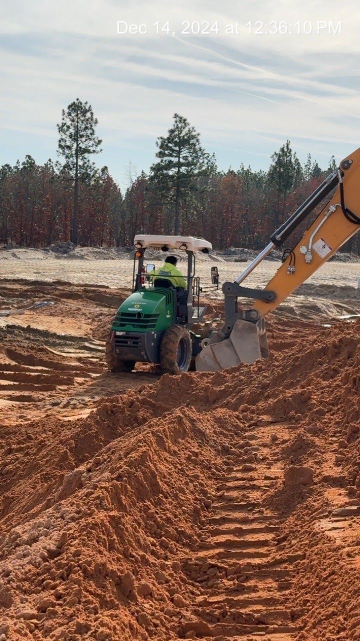 Green excavator digging in red dirt; a construction site.