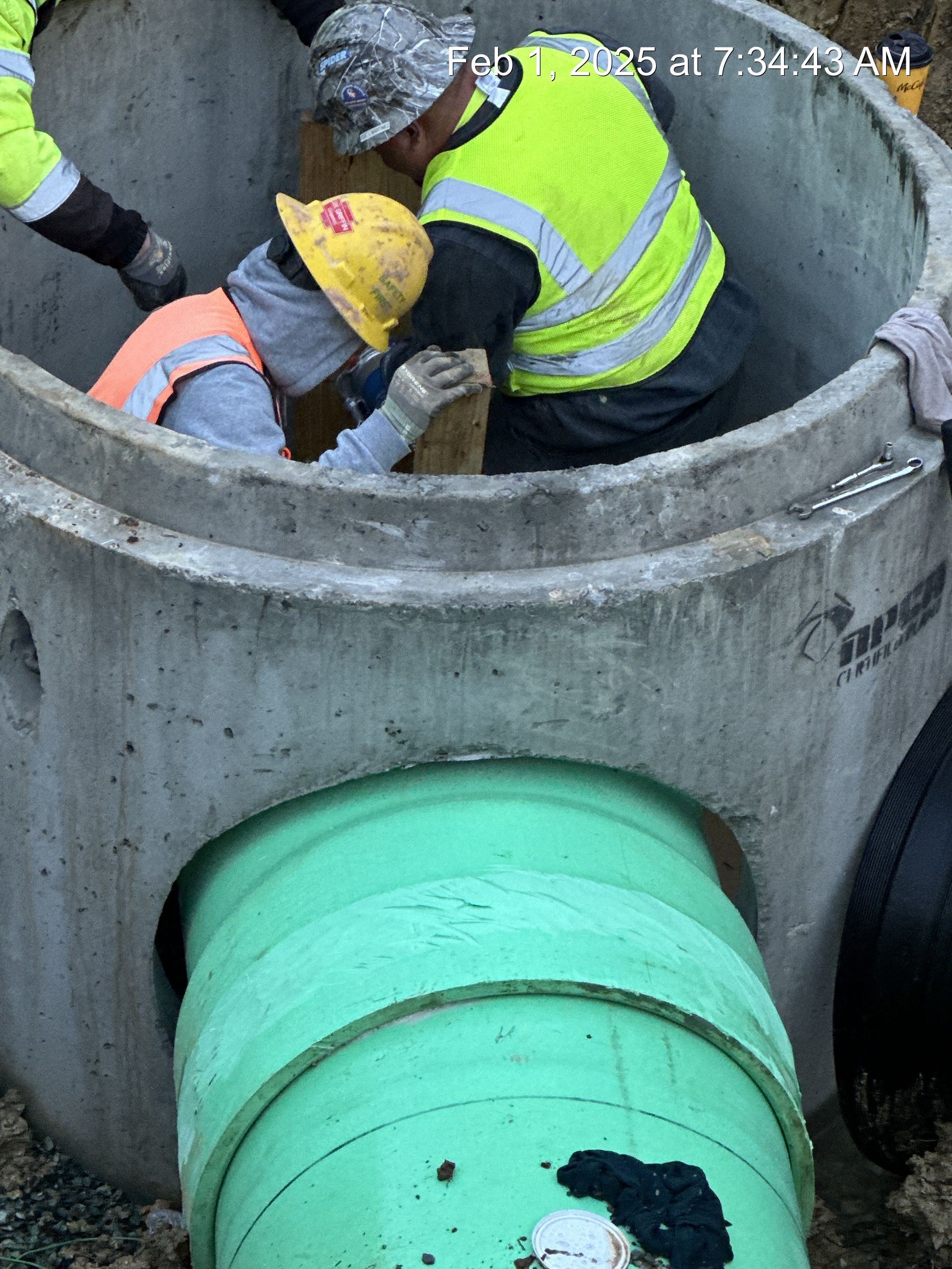 Construction workers installing a green pipe into a concrete structure.