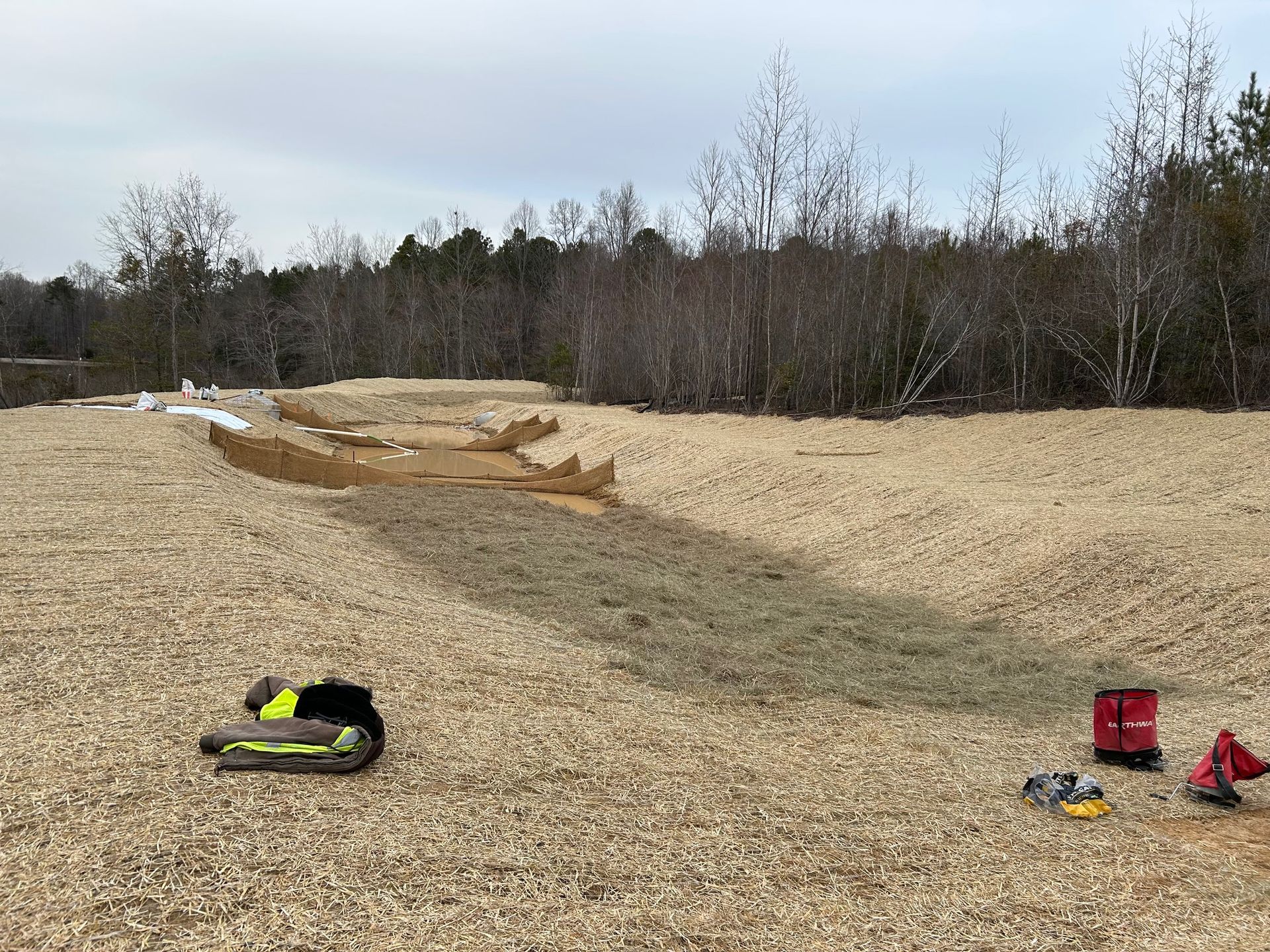 A sandy play area with toy construction vehicles; trees in the background under a cloudy sky.