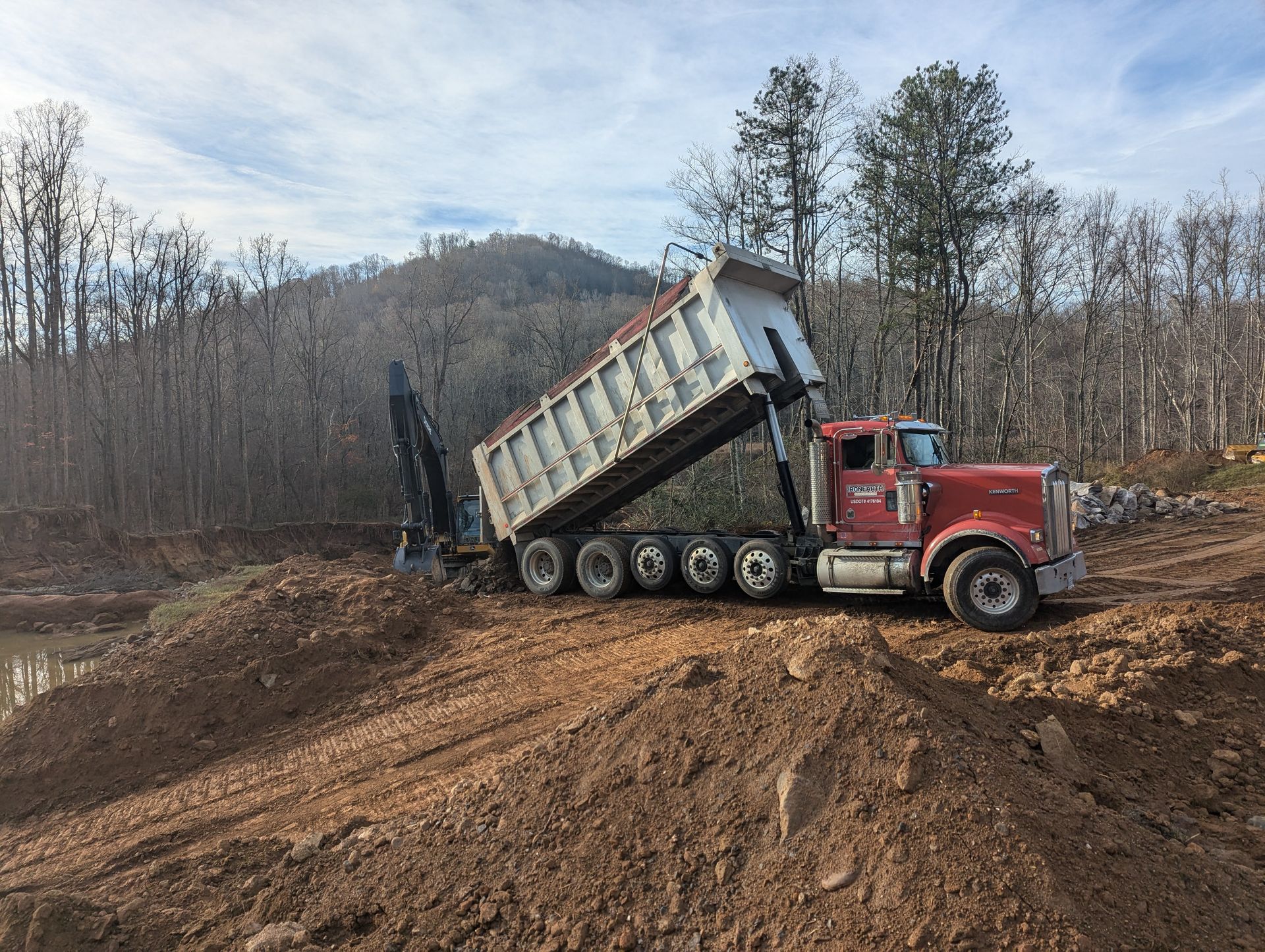 Red dump truck unloading dirt on a construction site near a forest.