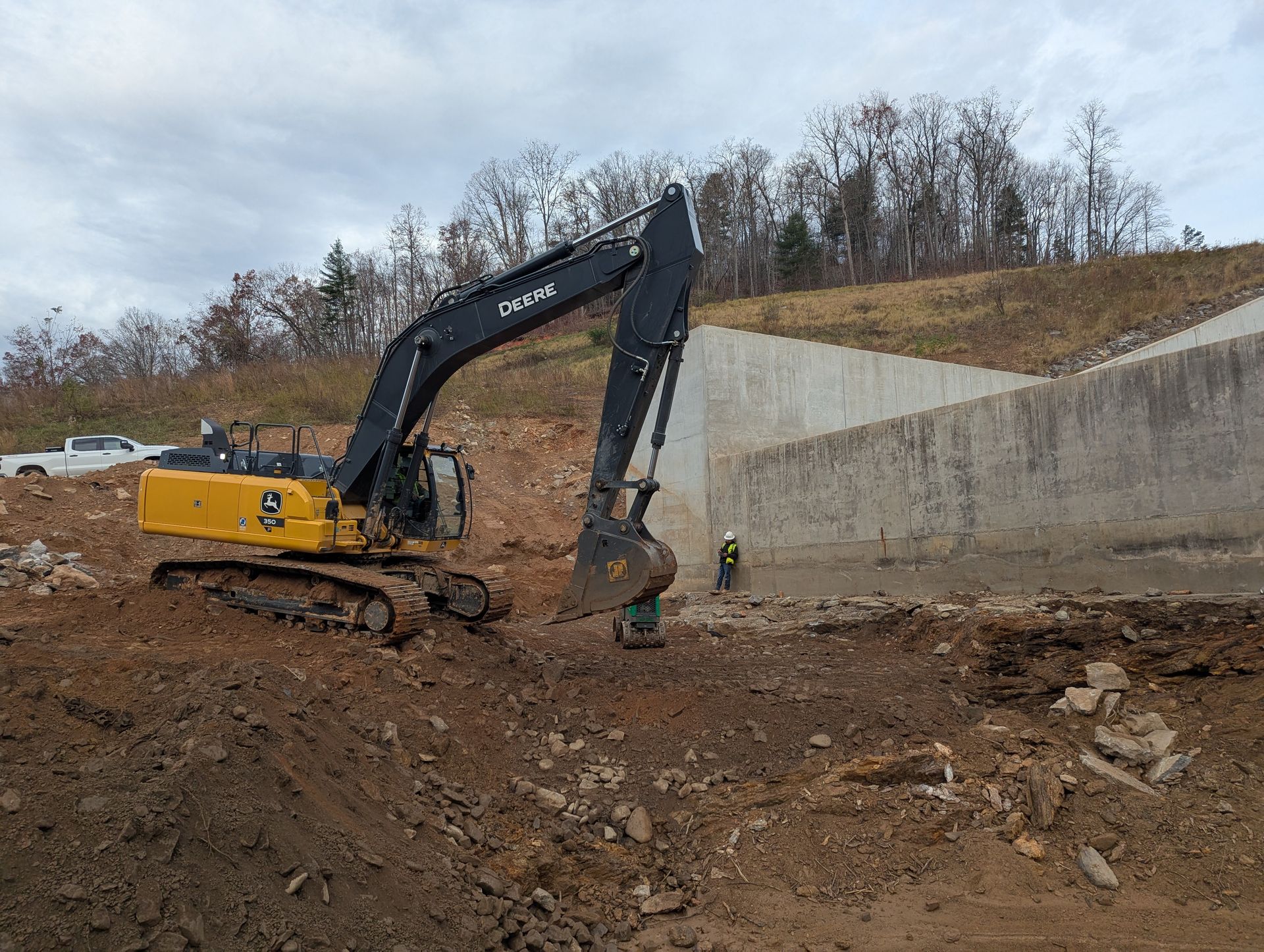 Yellow excavator digging near a concrete wall on a construction site, cloudy sky.