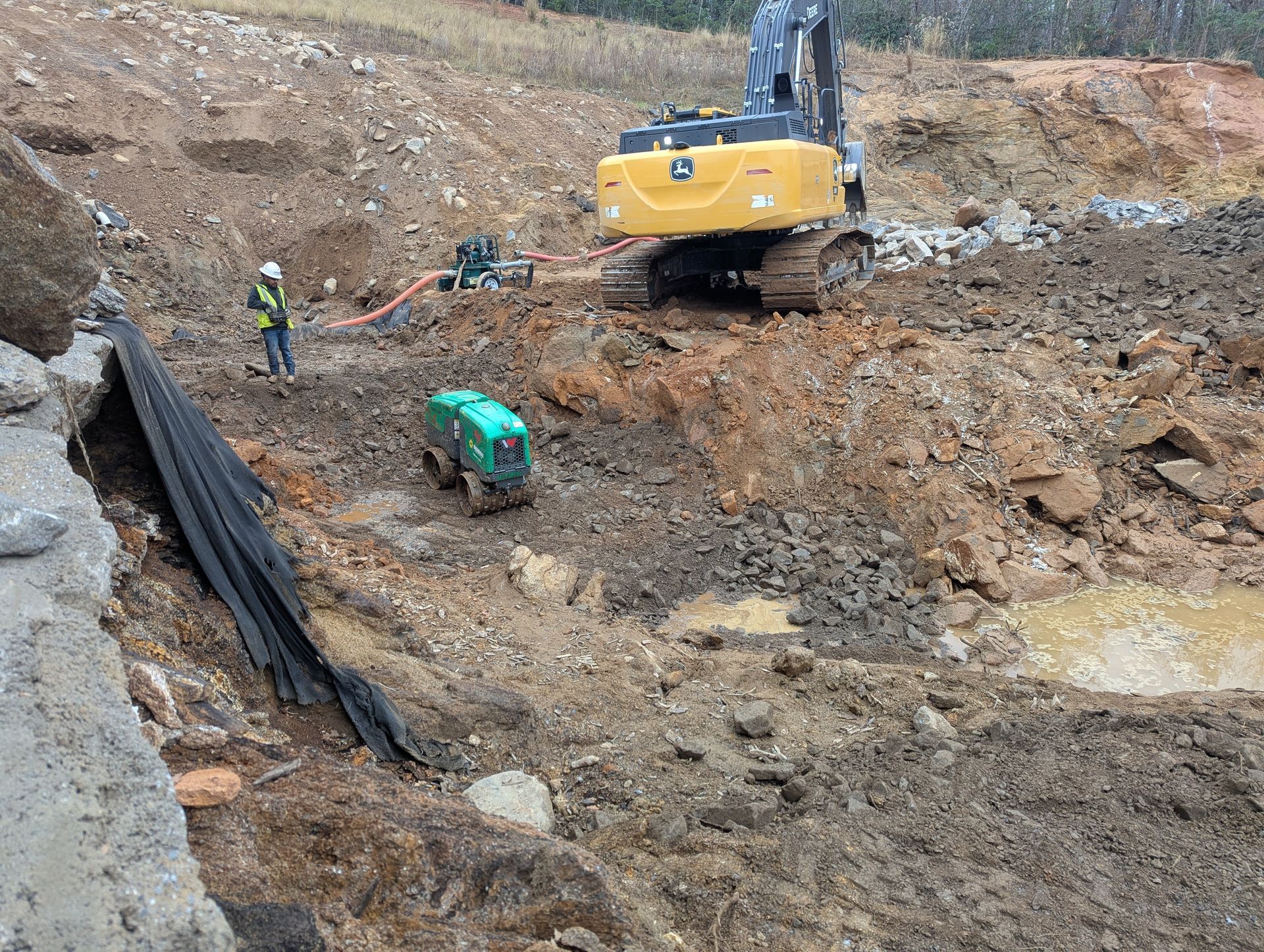 Construction site: excavator, worker, small green vehicle, and muddy terrain.