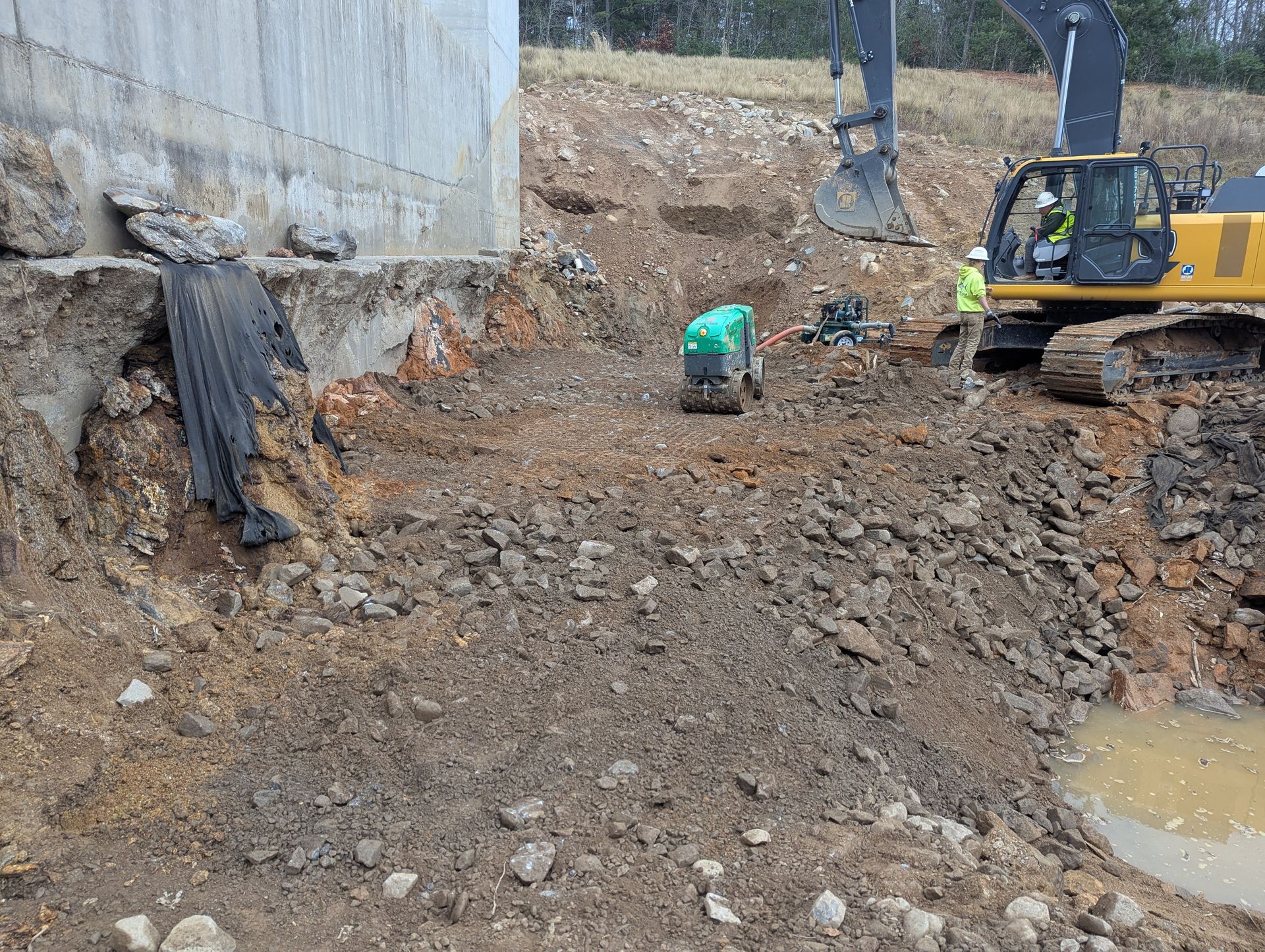 Construction site: Excavator near a concrete structure; workers, soil, rocks.
