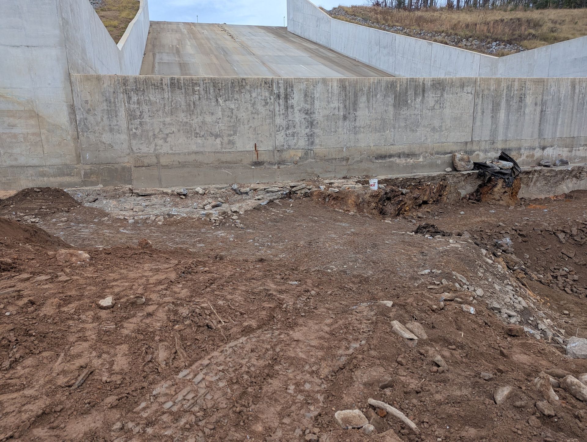 Concrete construction site: ramp descending, brown soil in foreground, walls on either side.