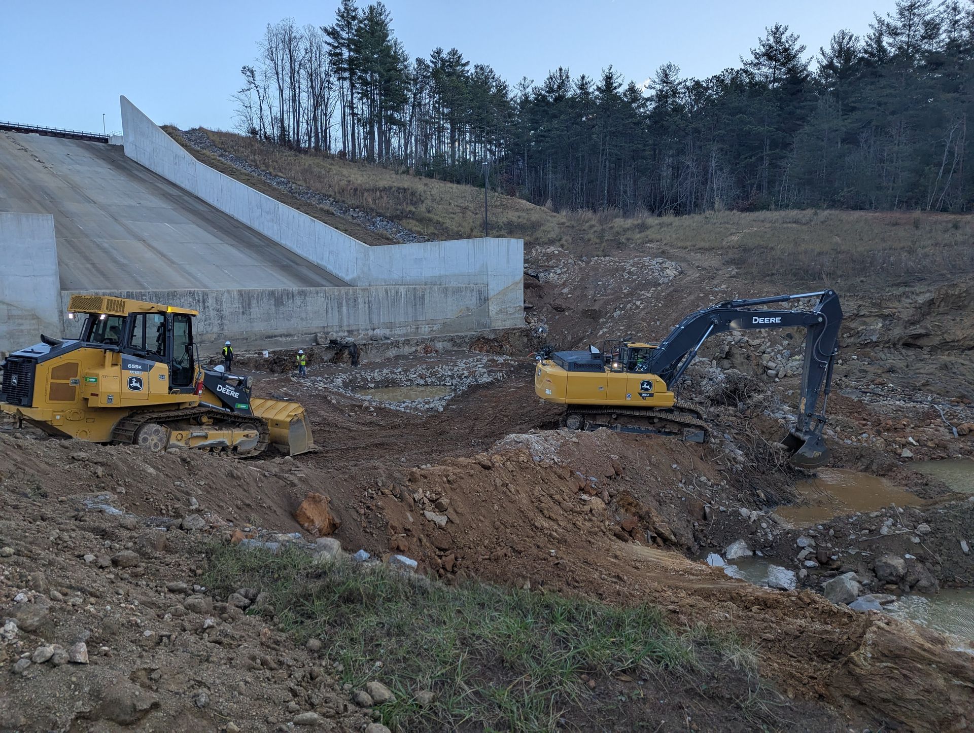 A bulldozer and excavator working at a construction site with a concrete retaining wall.