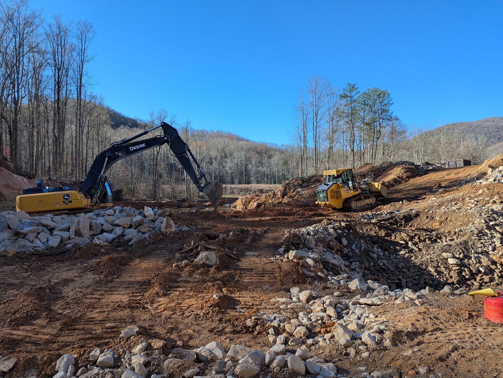 Construction site: Excavator and bulldozer moving earth and rocks on a hillside under a blue sky.