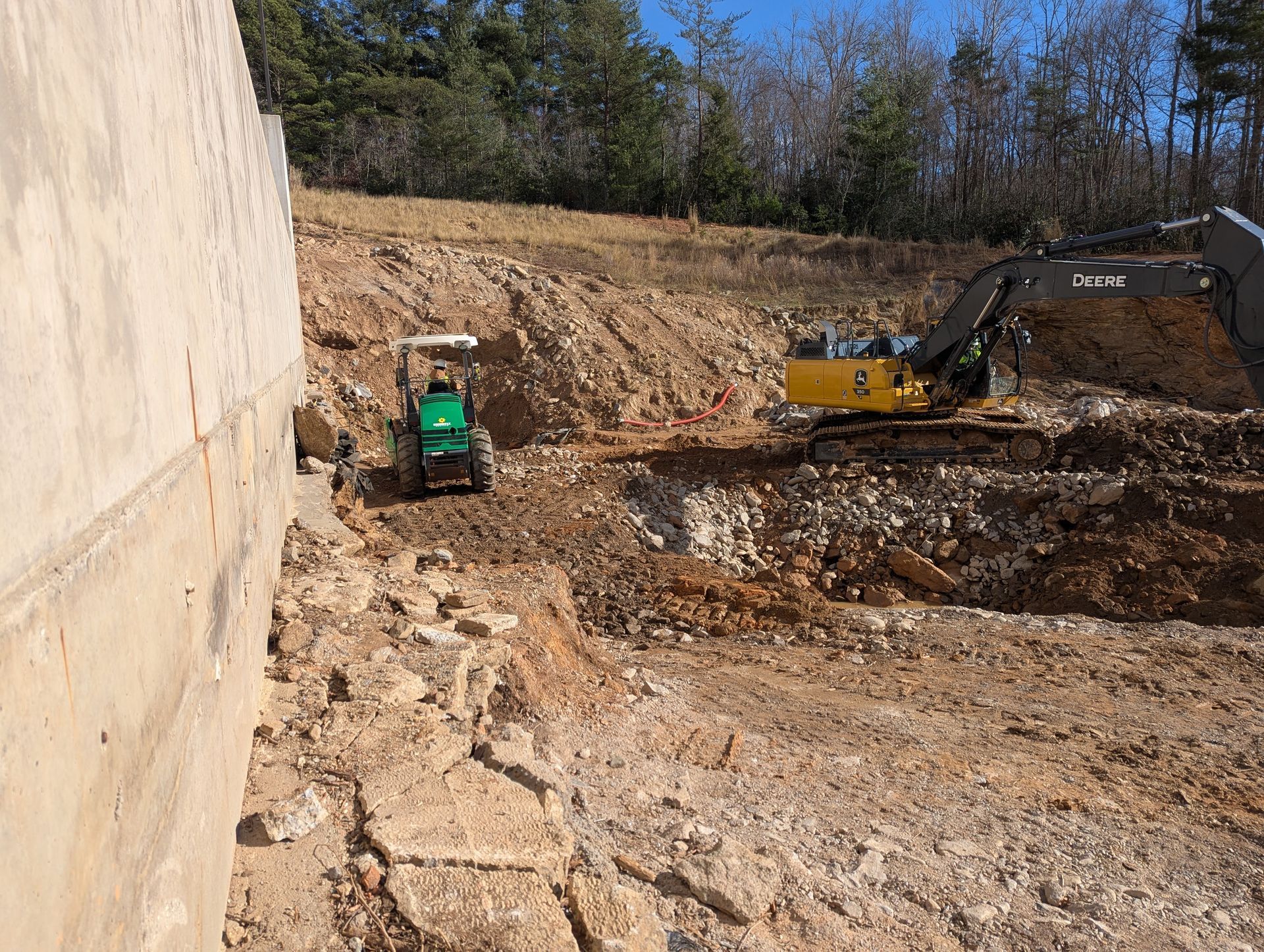 Construction site with excavator and skid steer removing dirt and rocks.