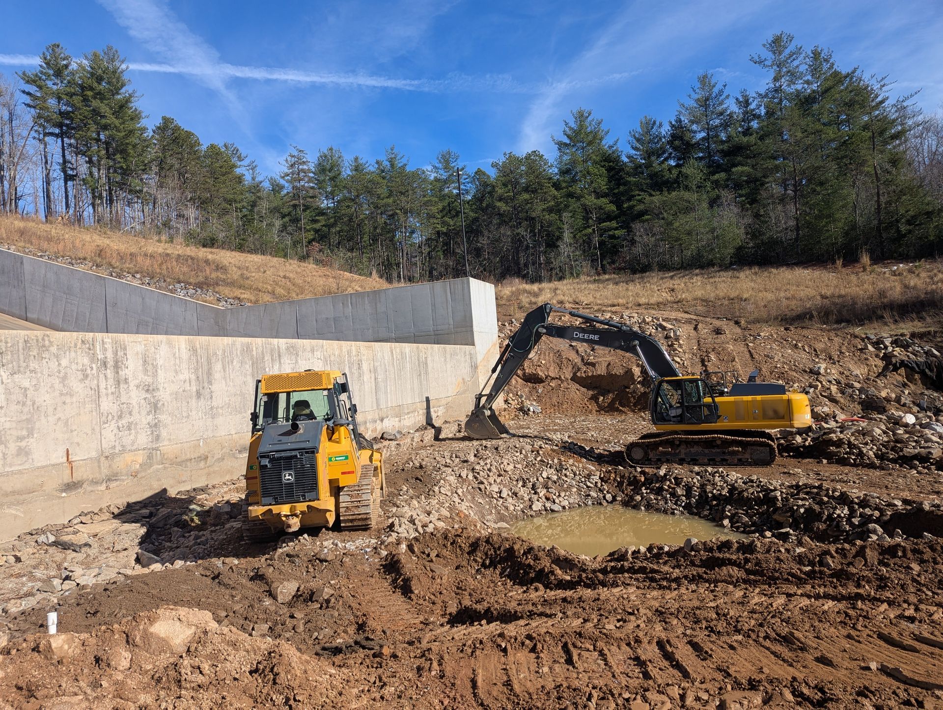 Construction site with two yellow excavators, dirt, and concrete retaining wall.