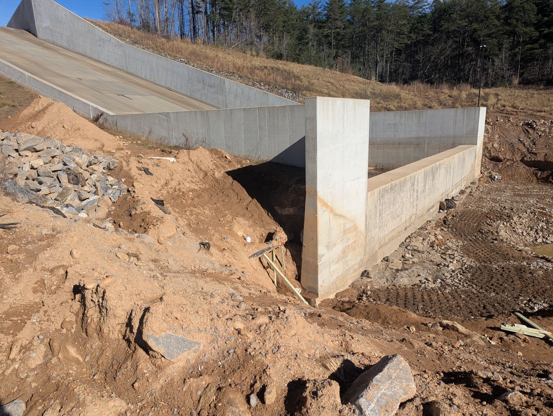 Concrete construction on a hillside with exposed dirt, rocks, and a ramp.