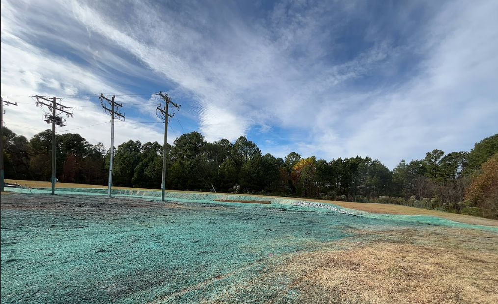 Field with three utility poles, newly seeded with blue-green spray, under a partly cloudy sky.