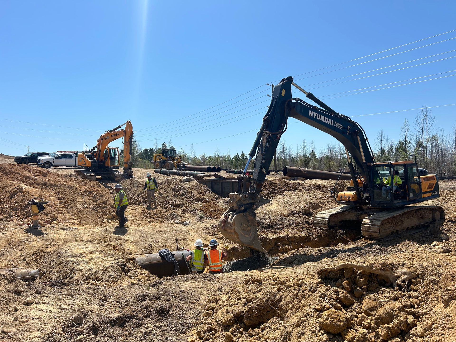 Construction site with excavators and workers in trenches under a clear blue sky.