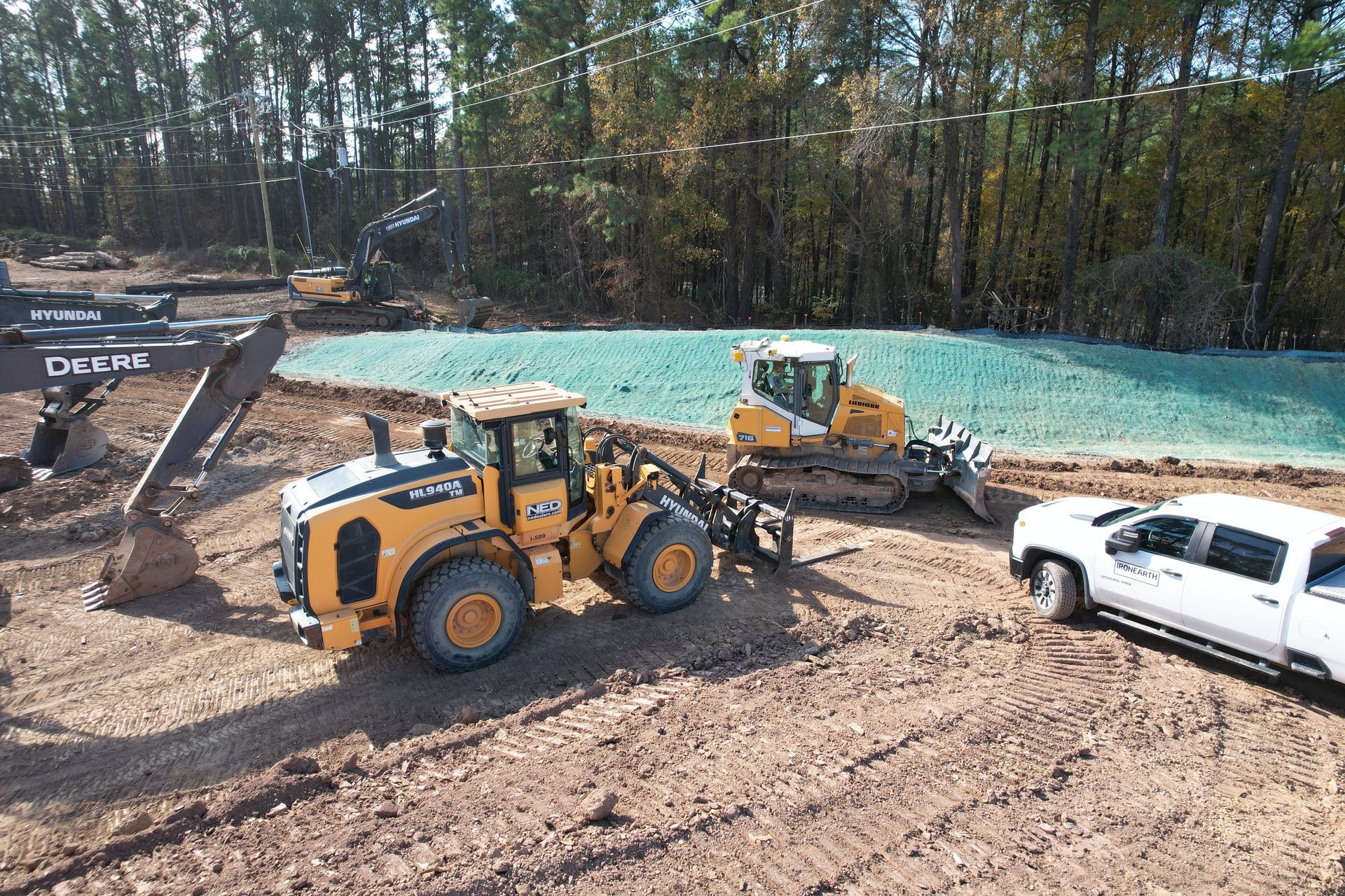 Construction site with a red dump truck unloading dirt near a pond and a worker observing.