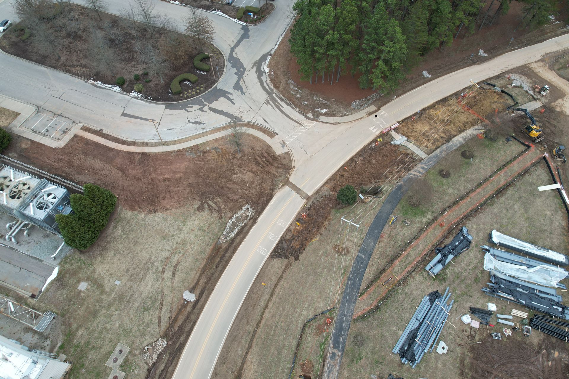 A John Deere excavator digs into dirt near a concrete structure at a construction site in a wooded area.