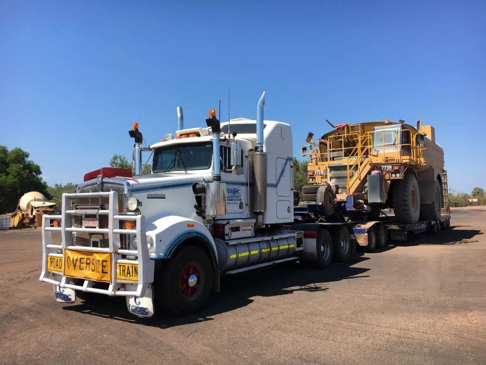 A Large White Semi Truck is Carrying a Large Yellow Excavator — Ostojic Group in Berrimah, NT