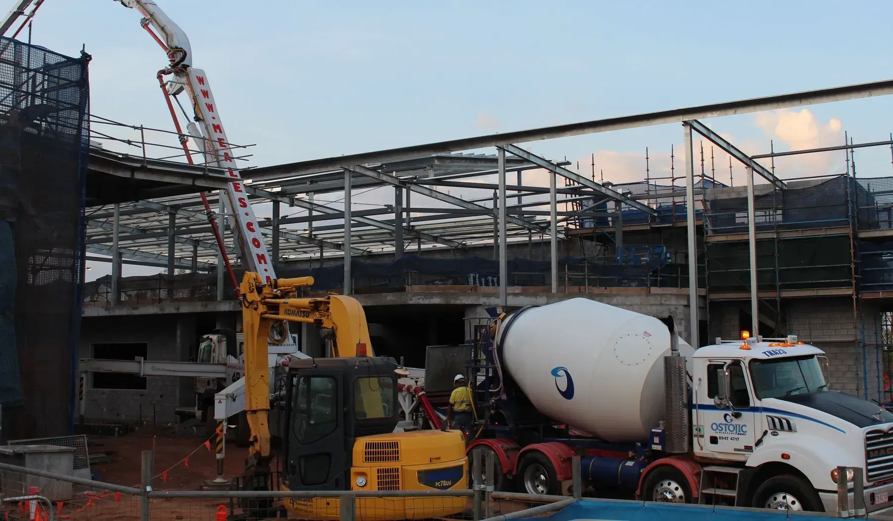 Construction Site With a Cement Truck, Excavator, and Workers, Pouring Concrete Into a Building Frame — Ostojic Group in Berrimah, NT